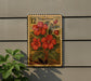 A wooden sign with a floral design hangs on a wall, featuring a large red flower surrounded by green leaves.