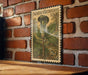 A vintage-style postage stamp featuring a large illustration of a flower, mounted on a brick wall.