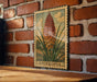 A vintage-style metal stamp depicting a kniphofia flower is displayed on a brick wall.