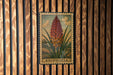 A metal stamp with a floral illustration and the word "KNIPHOFIA" printed on it, hanging on a wooden wall.