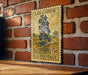 A vintage-style postage stamp from Larkspur, featuring a blue flower illustration, is displayed on a brick wall.