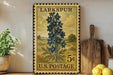 A vintage-style postage stamp from Larkspur, featuring a blue flower illustration, is displayed on a shelf next to a wooden cutting board and some kitchen utensils.