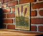 A framed illustration of three pink flowers is hanging on a brick wall, with the text "LIATRIS BLAZING STAR" below the image.