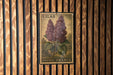A vintage postage stamp featuring a depiction of purple lilac flowers, mounted on a wooden wall.
