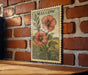 A framed illustration of two red flowers is hanging on a brick wall.