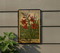 A framed image of red flowers is mounted on a wall, with a plant visible to the left.