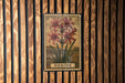 A framed illustration of a lily flower is hanging on a wooden wall.