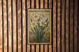 A framed image of a daffodil flower is hanging on a wooden wall.