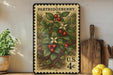 A vintage postage stamp featuring a detailed illustration of a berry plant, with the text "PARTRIDGEBERRY" and "U.S. 4c" printed on it. The stamp is displayed on a shelf next to a wooden cutting board and a potted plant.