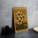 A framed illustration of a peacock orchid plant with yellow flowers, placed on a gray countertop next to a stack of black camera lenses.