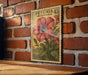 A vintage-style stamp depicting a large pink flower is displayed on a brick wall, with a wooden table below it.