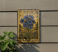 A vintage U.S. postage stamp featuring a blue wild blue flower is displayed on a wall, with a plant to the left.