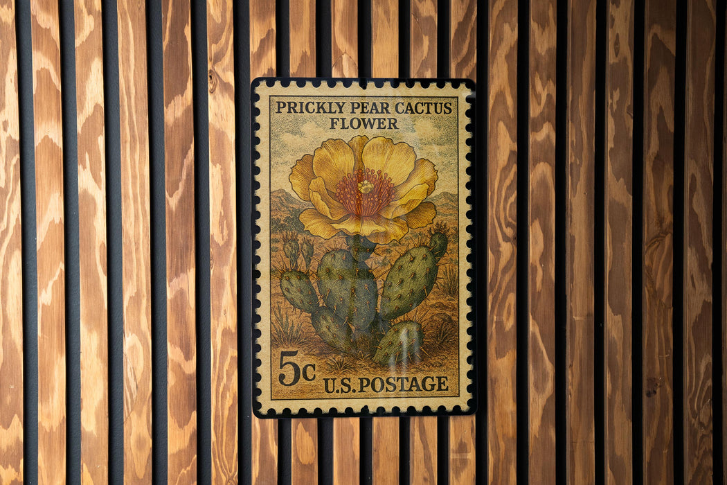 A U.S. postage stamp featuring a Prickly Pear Cactus Flower, mounted on a wooden wall.