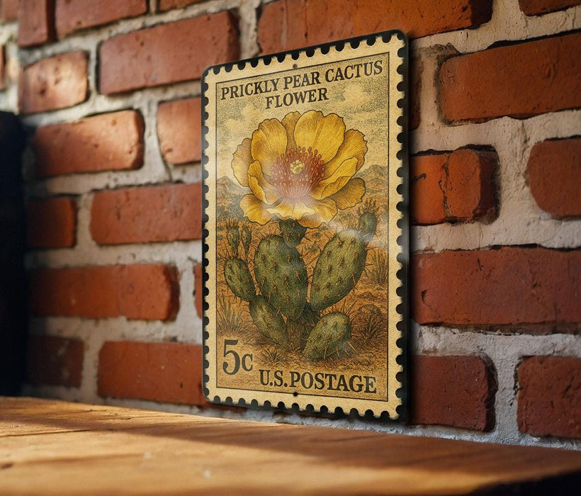 A vintage U.S. postage stamp featuring a yellow pear cactus flower is displayed on a brick wall.