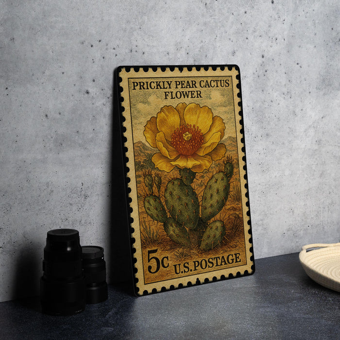 A 5c U.S. postage stamp featuring a Prickly Pear Cactus flower, placed on a gray countertop next to some black camera lenses.