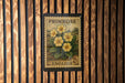 A vintage-style postage stamp from the United Kingdom, featuring a floral design with yellow flowers, mounted on a wooden wall.