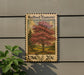 A wooden postcard-style stamp depicting a redbud tree, with the text "Redbud (Eastern)" and "USA 20c" printed on it, mounted on a wall next to a plant.