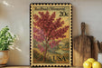 A framed postcard with a vibrant illustration of a redbud tree, placed on a shelf next to a wooden cutting board and a potted plant.