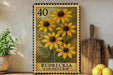 A framed print of a yellow flower with the text "Rudbeckia 'Goldstorm'", placed on a shelf next to a wooden cutting board and a potted plant.