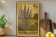 a framed stamp with a floral design, placed on a shelf next to a wooden cutting board and some potted plants.