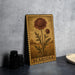 a wooden frame with a floral illustration of a scabiosa flower, which is a type of flower. The frame is placed on a gray surface, and there are some black camera lenses visible in the background.