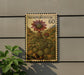 a postage stamp with a floral design, mounted on a wall next to a plant.