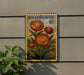 a stamp-like artwork depicting a vibrant red flower with green leaves, mounted on a wall.