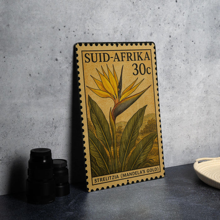A metal stamp with a yellow flower and green leaves, labeled "Süid-afrika 30c STREITZIA (MANDELA'S GOLD)" on a gray wall.