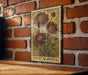 A vintage-style floral print is displayed on a brick wall, featuring a large flower with three petals and a smaller flower below it.