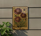 a decorative metal sign with a floral design, mounted on a wall next to a plant.