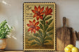 A framed stamp-like artwork depicting a cactus plant with red flowers, placed on a shelf next to a wooden cutting board and some lemons.