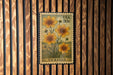 A US postage stamp featuring a floral design with yellow flowers, mounted on a wooden wall.