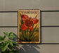 A framed illustration of a red flower with green leaves, mounted on a wall next to a plant.