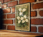 A vintage-style postage stamp featuring a white trillium flower is displayed on a brick wall.
