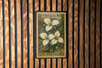 A framed postage stamp featuring a white flower on a wooden background.