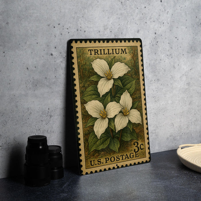 A metal stamp with a floral design, featuring three white trillium flowers, is displayed on a table next to a stack of black camera lenses.