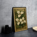 A metal stamp with a floral design, featuring three white trillium flowers, is displayed on a table next to a stack of black camera lenses.
