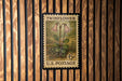 A vintage U.S. postage stamp featuring a floral illustration of two pink flowers on a green background, mounted on a wooden wall.