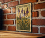 a framed illustration of purple flowers on a brick wall, with the word "VERVAIN" written on the frame.