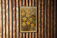 A vintage-style postage stamp featuring a floral design with yellow flowers, mounted on a wooden wall.