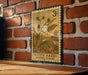 A vintage-style stamp depicting a witch hazel plant, with the text "Witch Hazel (Winter Bloom)" printed on it, is displayed on a brick wall.
