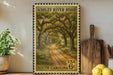 A framed vintage postage stamp depicting a scenic road through a lush, wooded area, with the text "ASHLEY RIVER ROAD" and "USA 6c SOUTH CAROLINA" printed on it. The stamp is displayed on a shelf next to a wooden cutting board and a potted plant.