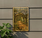 A vintage-style postage stamp depicting a scenic road lined with trees, mounted on a wall next to a plant.