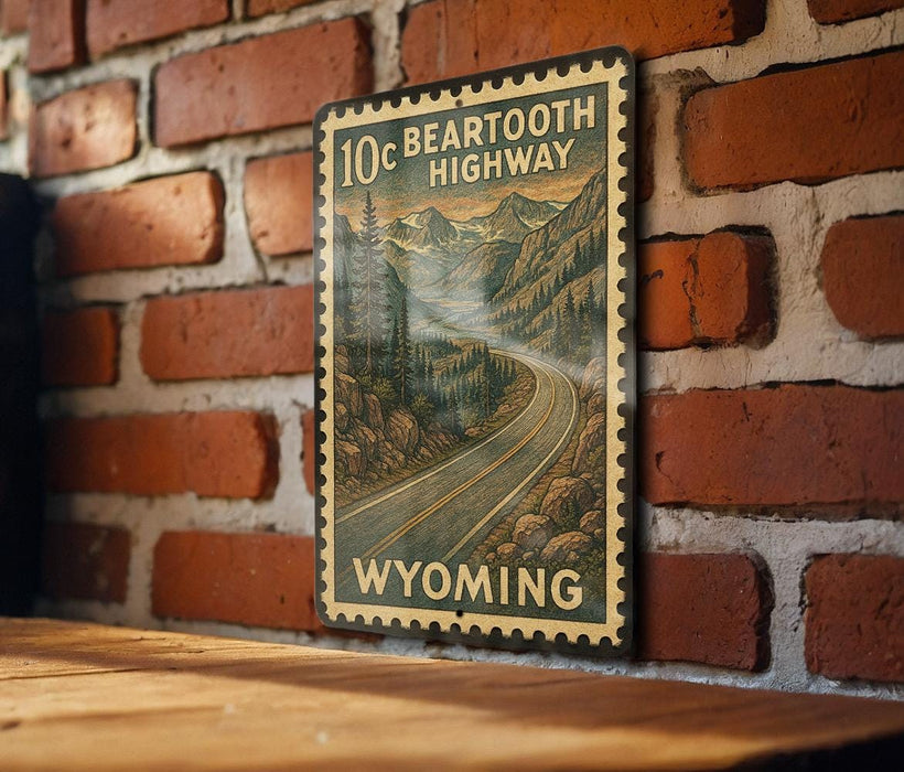 A vintage-style metal sign with a mountain landscape and a winding road, mounted on a brick wall.
