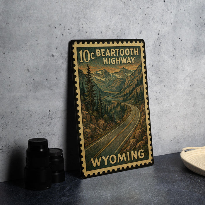A vintage-style metal sign with a scenic mountain landscape and a winding road, depicting the 10 C. Bear Tooth Highway in Wyoming.