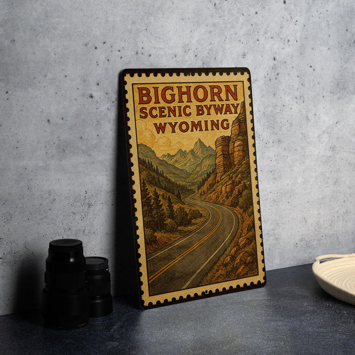 A framed poster of the scenic route in Wyoming, featuring a winding road surrounded by mountains and forests.