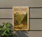 A 10-cent U.S. postage stamp from Wyoming, featuring a scenic mountain landscape, is displayed on a wall next to a plant.