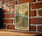 A framed illustration of a coastal road in Wisconsin, with a scenic landscape of trees, water, and mountains.