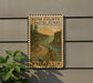 A wooden sign with a scenic coastal landscape, featuring a winding road and a body of water, mounted on a wall.