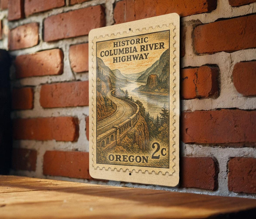 A wooden surface with a brick wall in the background, featuring a vintage-style postage stamp depicting the historic Columbia River Highway in Oregon.
